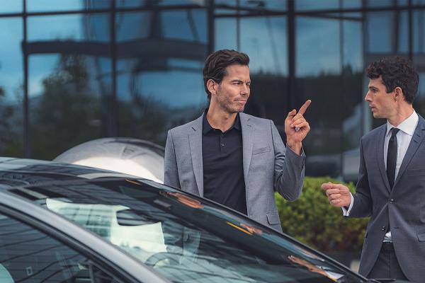 This is Audi — Audi Two young men standing behind an Audi car. They are both wearing suits. The man on the left is point his finger at the man on the right.