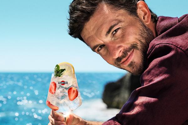 Off Script - MARTINI Actor Jonathan Bailey smiling at the camera holding a Martini Spritz with the sea in the background