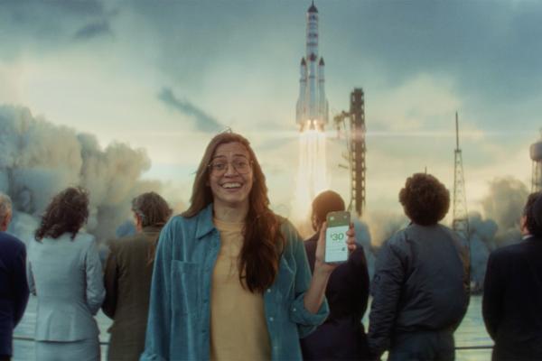 Woman holding up her phone facing the camera while a rocket launches in the background