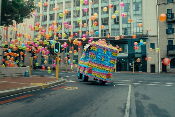 Life on the Mind — Volkswagen A car turrns down a street, in the background there are hundreds of colorful balloons