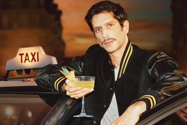 Sober Chic — Maison Perrier Young man holding a cocktail in one hand while leaning outside of the door of a taxi