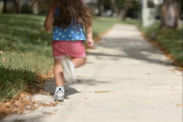 These Legs — Dove Shot from behind of a three eyar old girl in blue shirt and pink shorts running down a sidewalk