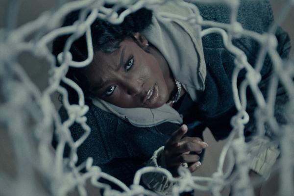 What it Takes — Powerade LSU athlete and hip hop artist Flau'jae Johnson looking up through the white netting of a basketball hoop, filmed from above