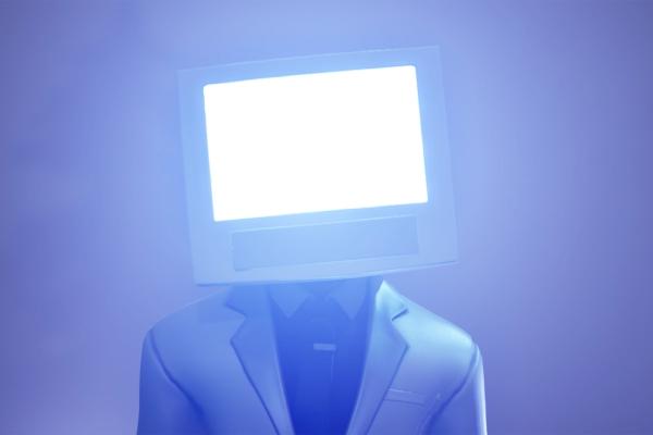 Screen Block — Vaseline Image of a person in a suit, with a monitor in place of a head. The monitor is on and emitting a bright light