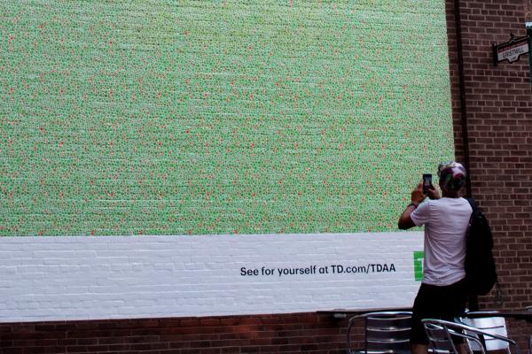 Person facing outdoor ad, the ad is made up of tiny green and white dots/pattern. 