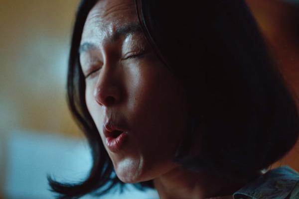 Hurts Real Good — Sprite A close-up shot of a person's face, with their eyes closed and mouth slightly open as if exhaling or making a sound. Their skin appears slightly sweaty or dewy, and their dark hair frames their face. The background is blurred with hints of light and shadow.